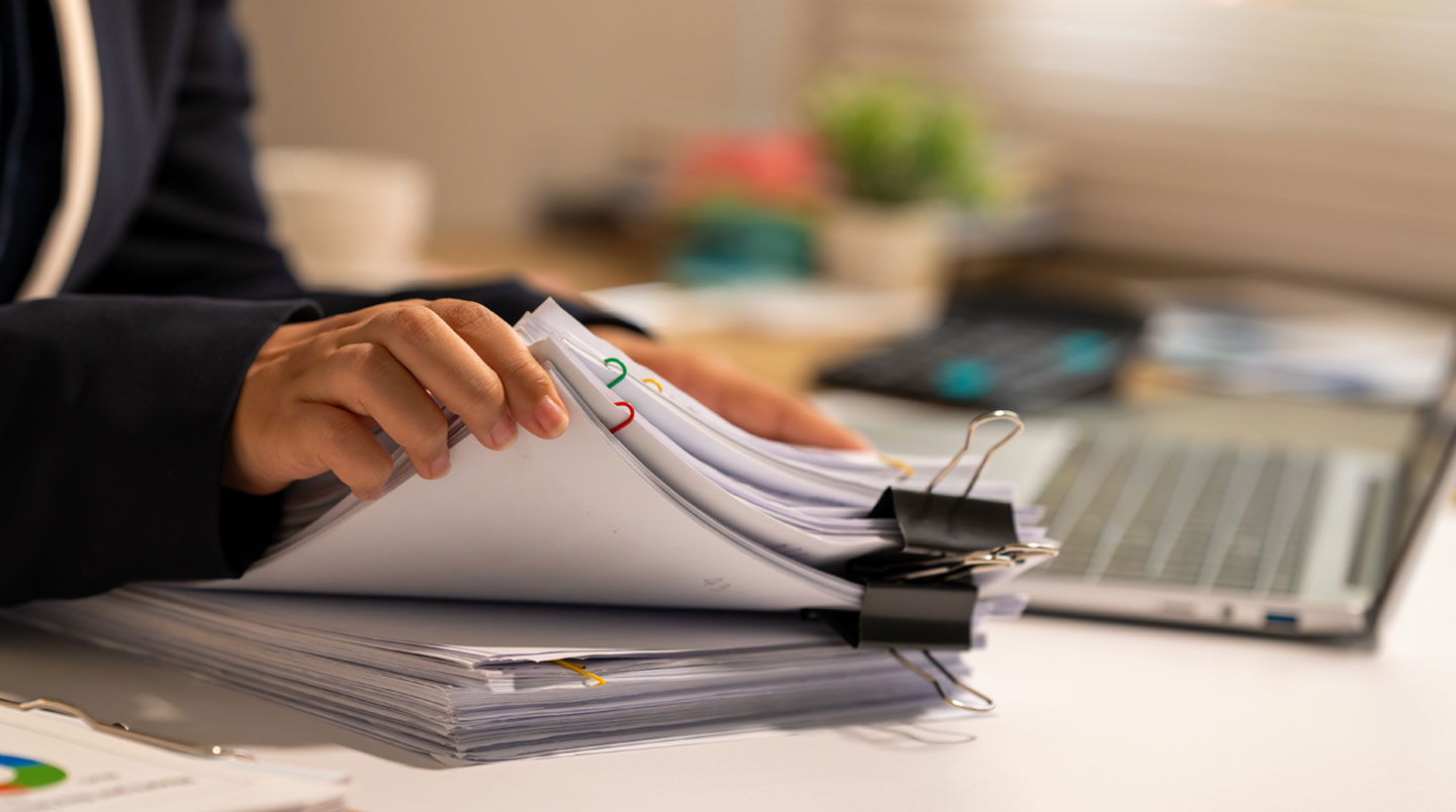 Bureau de comptabilité surchargé avec piles de factures papier, tableur Excel complexe ouvert sur l'écran, post-it et documents éparpillés illustrant la complexité de la gestion manuelle des relances